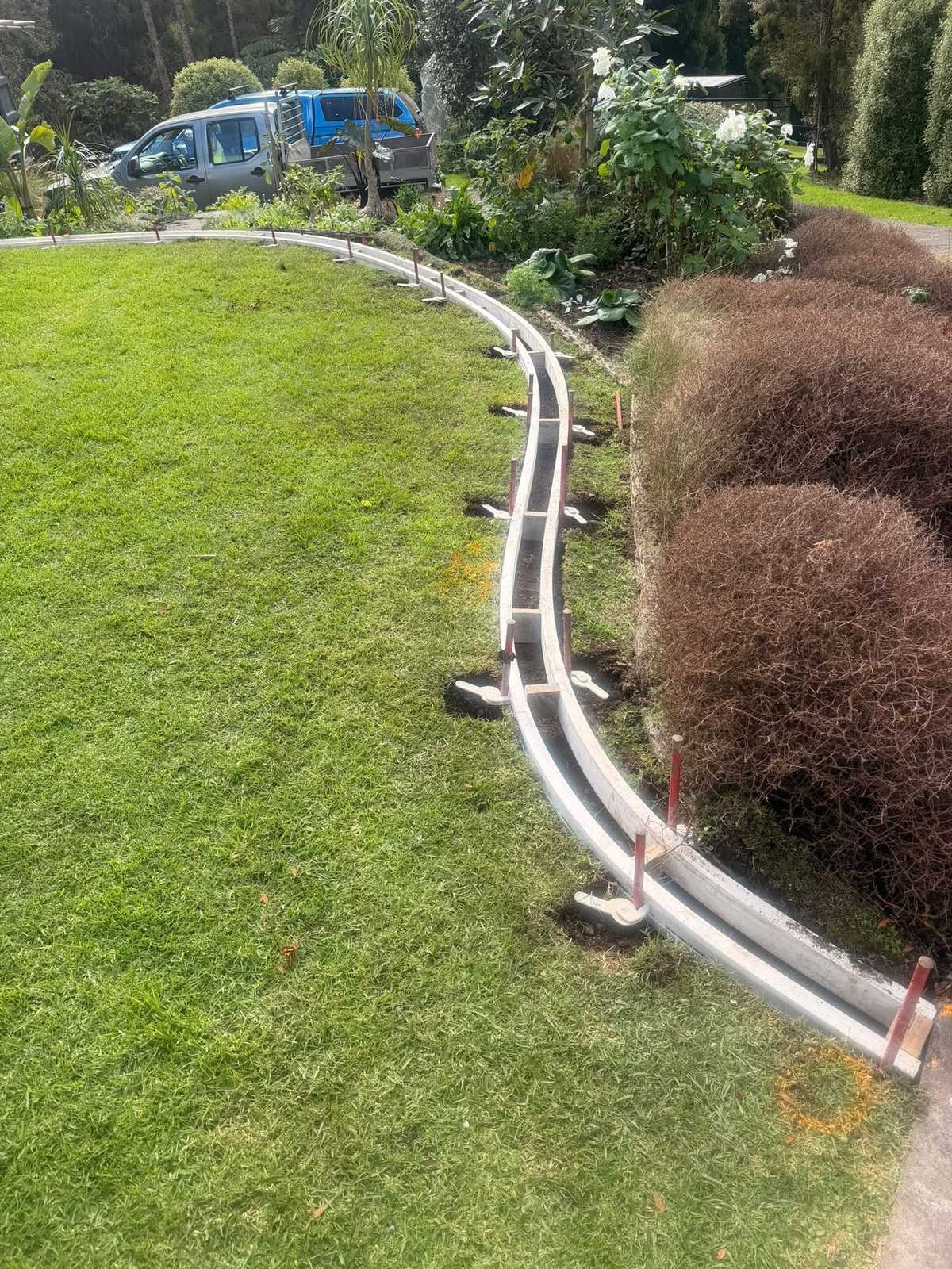 A long curved concrete garden edge poured between a green lawn and a planted border