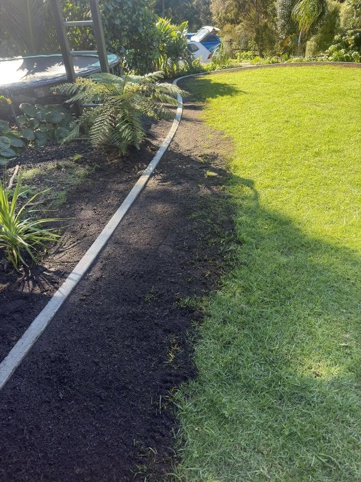 A freshly mulched dark garden bed beside a bright green lawn with a concrete edge